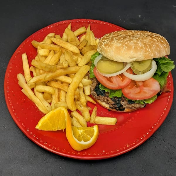 A grilled burger with lettuce, tomato, onion, and pickles, served with fries and orange slices.