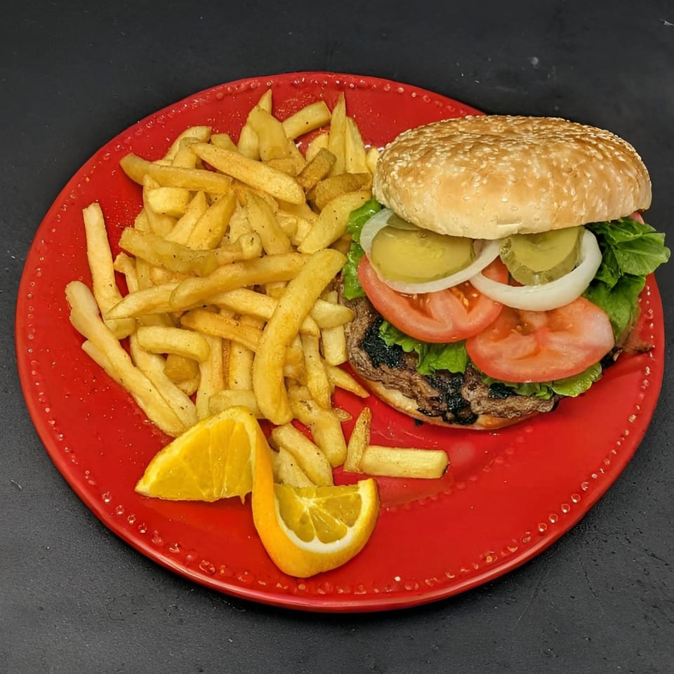 A grilled burger with lettuce, tomato, onion, and pickles, served with fries and orange slices.