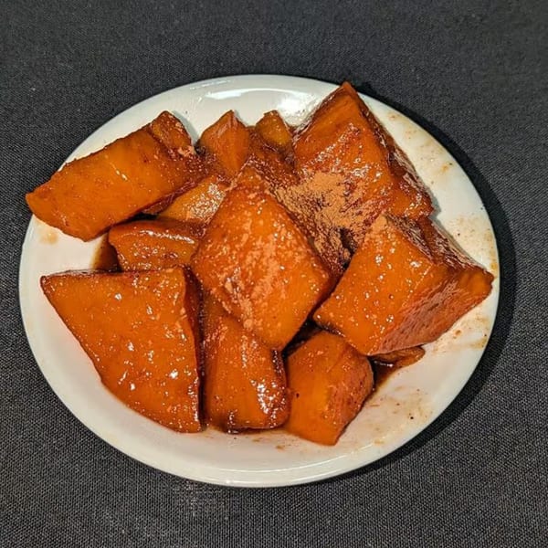 A white plate filled with glazed candied yams, sprinkled with cinnamon, from Charlie Staples Pitt Boss BBQ.