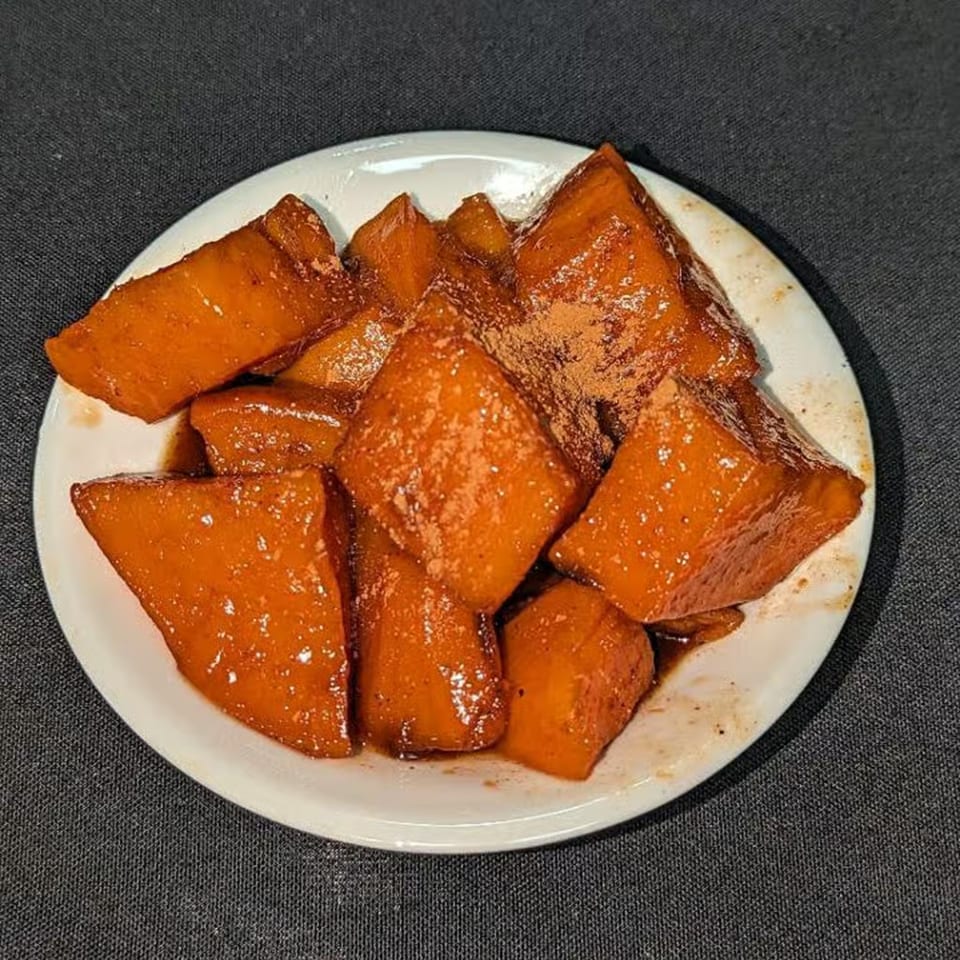 A white plate filled with glazed candied yams, sprinkled with cinnamon, from Charlie Staples Pitt Boss BBQ.