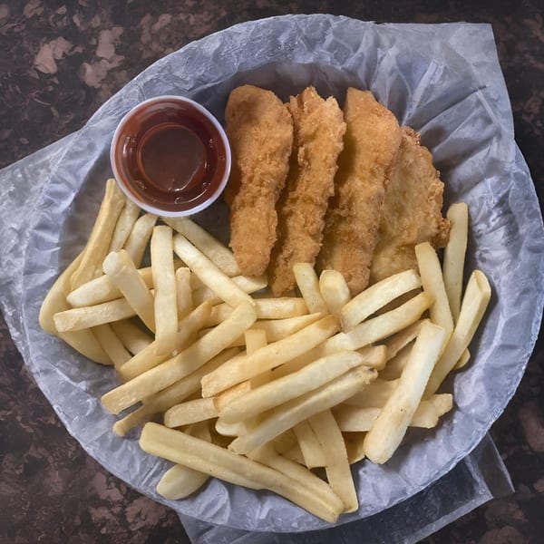 Crispy chicken tenders and golden french fries with a side of BBQ sauce in a paper-lined basket.